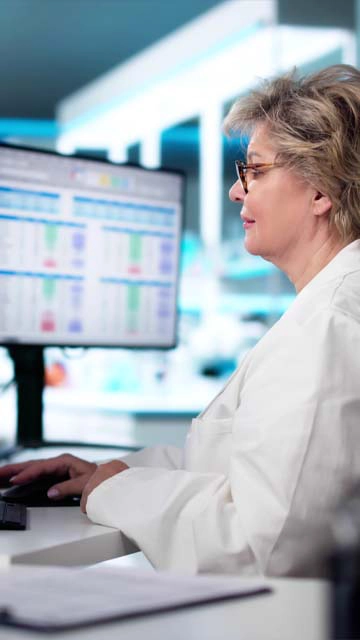 A researcher works with data on a computer in a lab wearing a white coat. Advance your career—learn more about our Bioinformatics Master’s Program!
