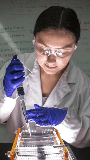 A person wearing a white jacket and blue gloves, holding a syringe and focusing intently on what they are doing.